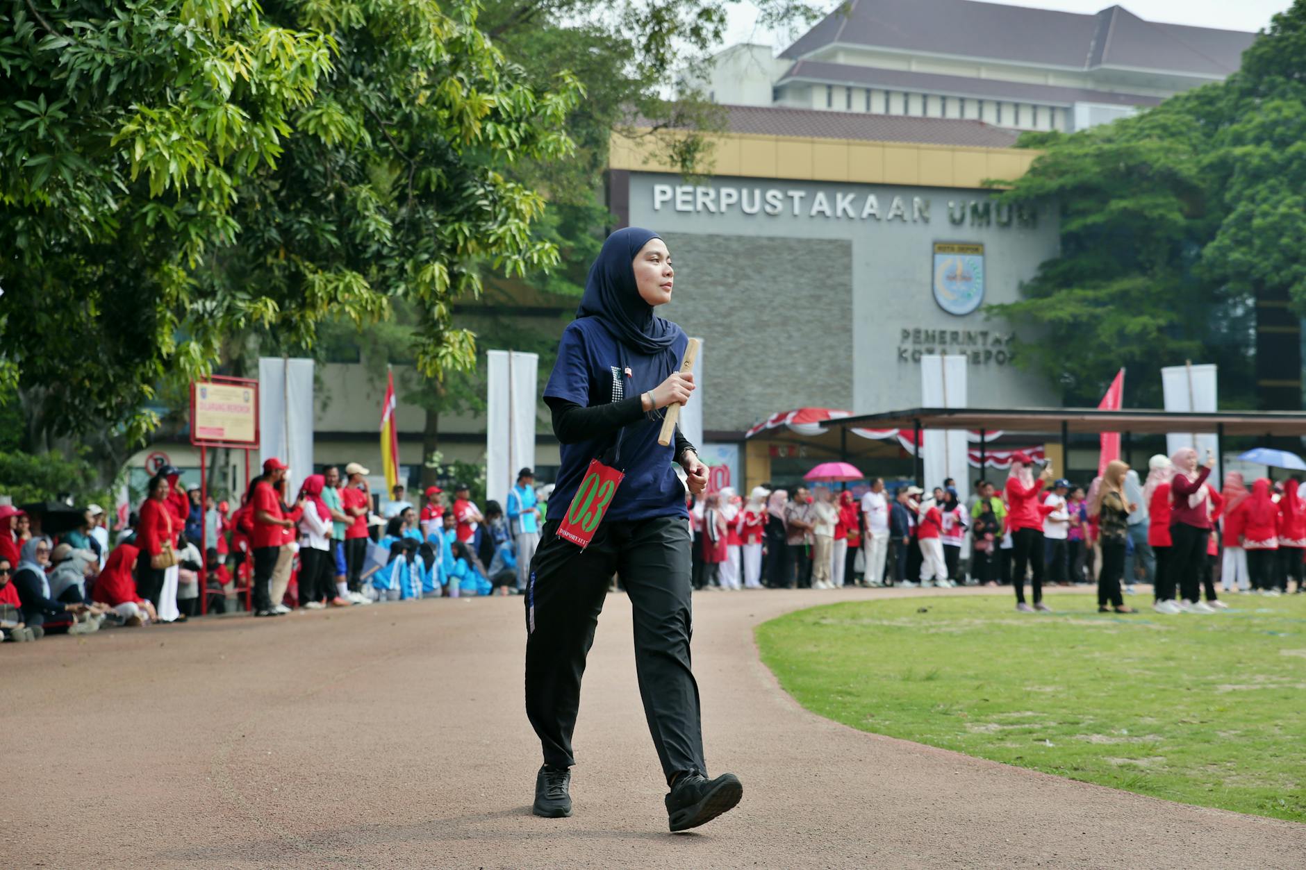 A young woman walking confidently at a lively community event held outdoors, with a crowd in the background.