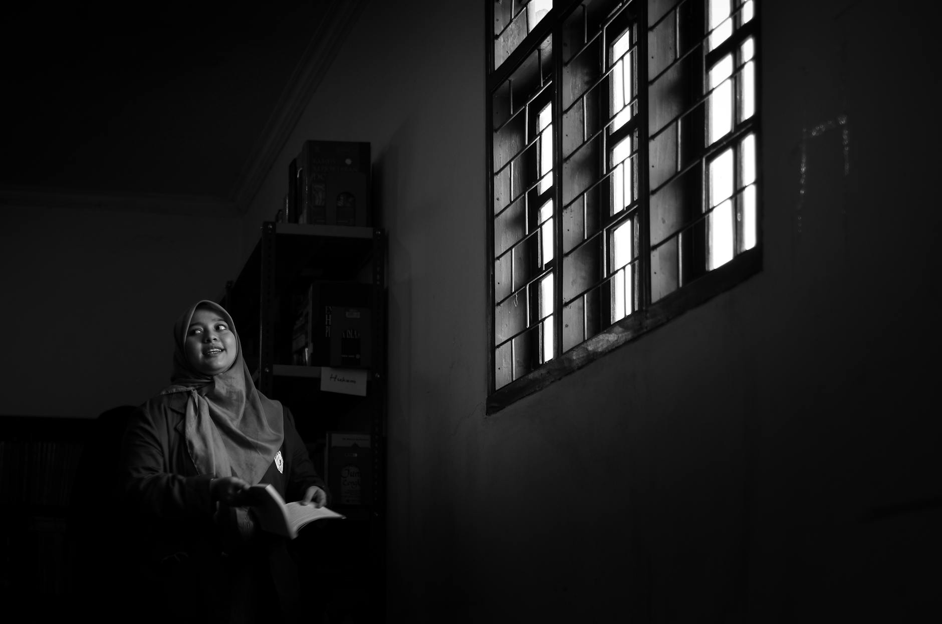 Black and white portrait of a woman in a dimly lit room, gazing thoughtfully.