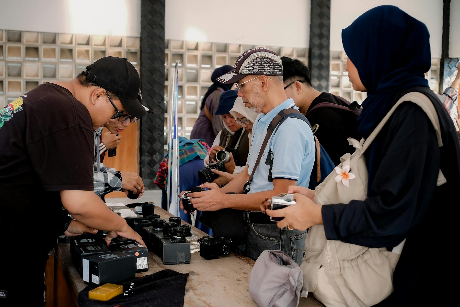 Group of people examining vintage cameras at a table indoors during the day.