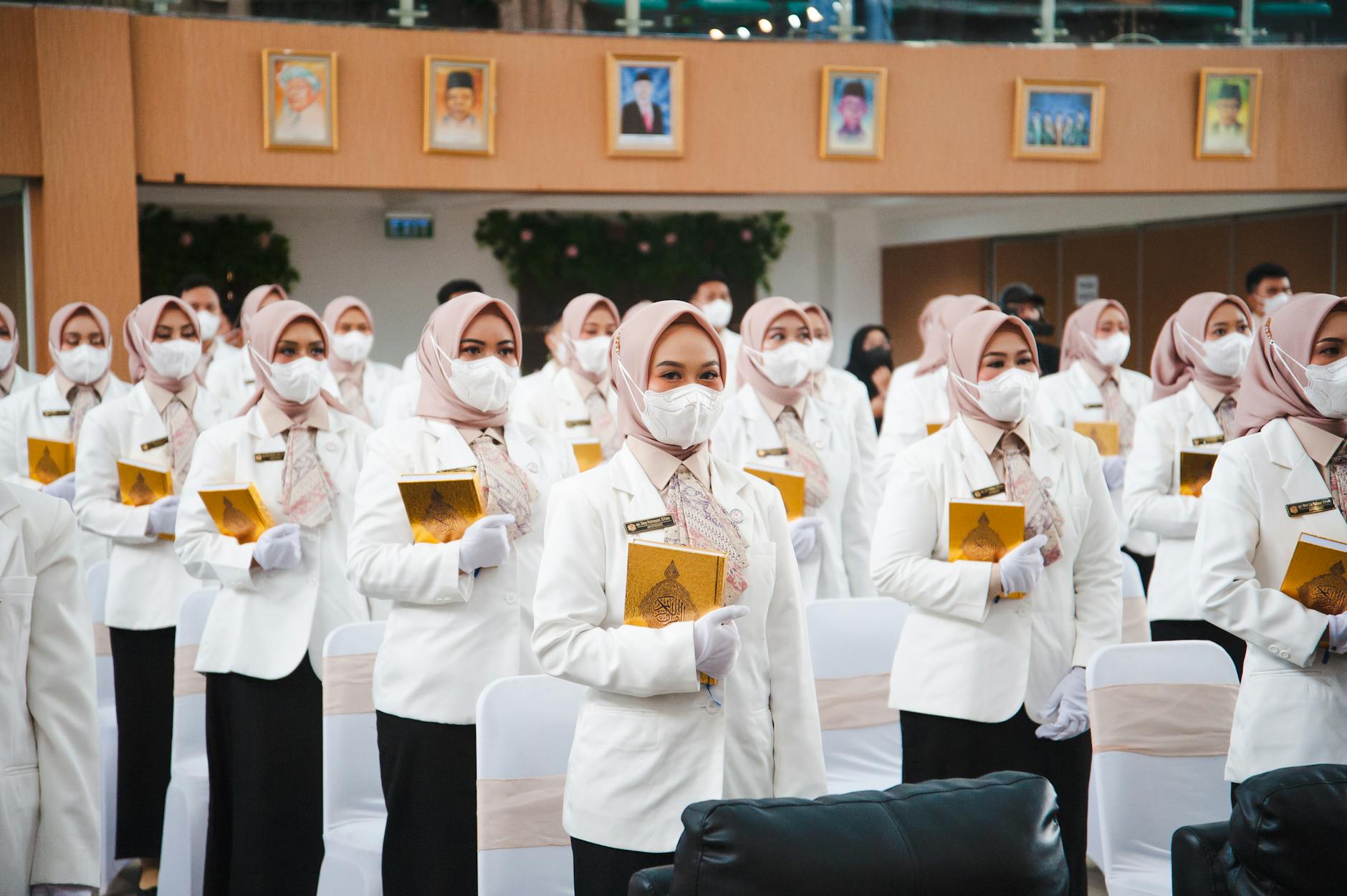 Muslim women in hijabs and masks during a graduation ceremony indoors.