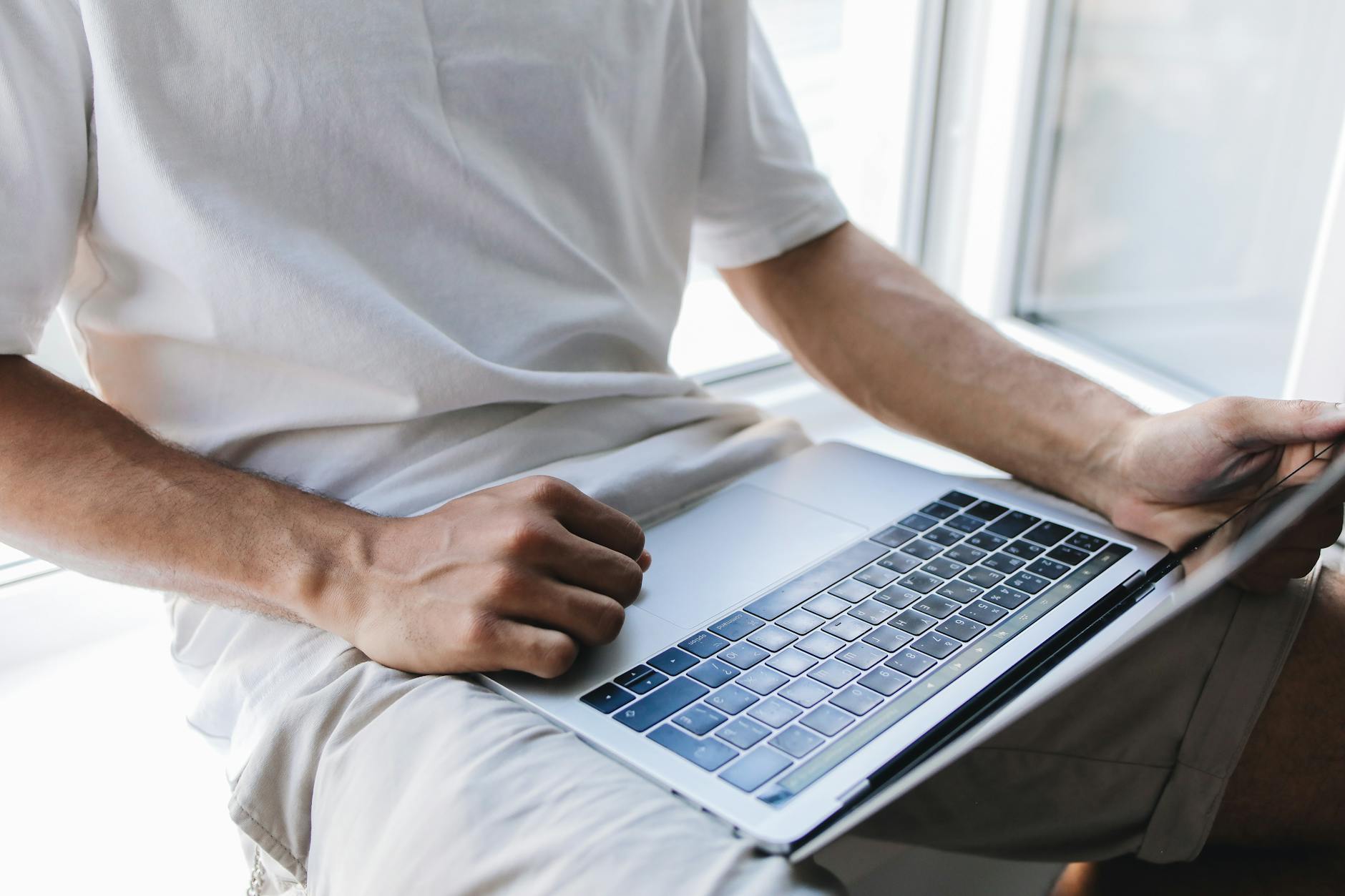 Close-up of a man using a laptop by a window, engaged in online study or work.