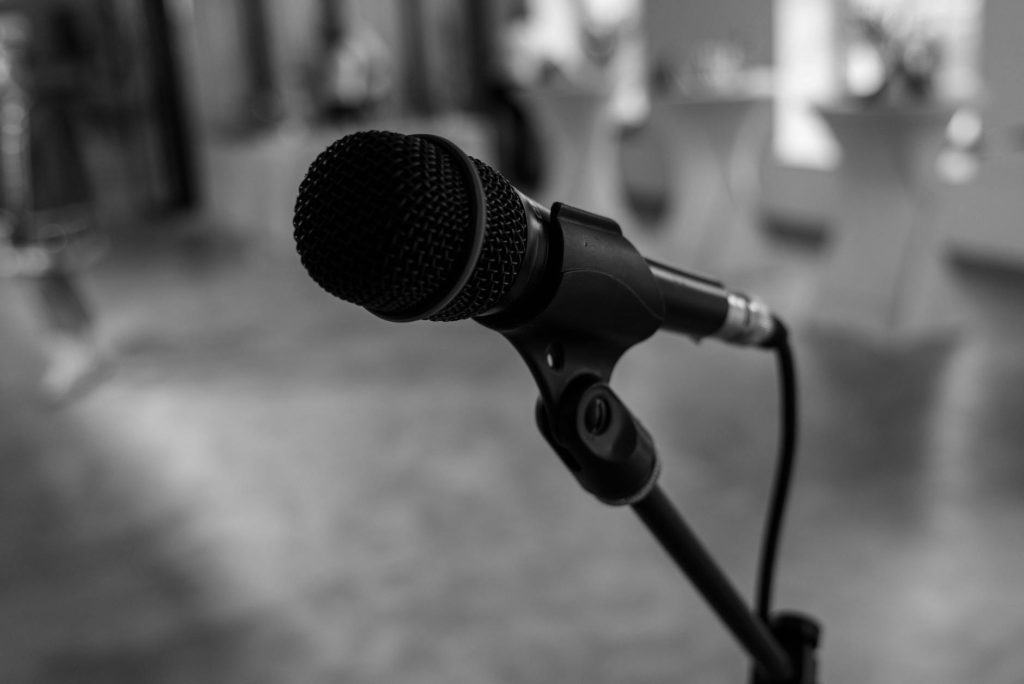 Detailed black and white close-up of a microphone in an indoor setting, capturing its texture.