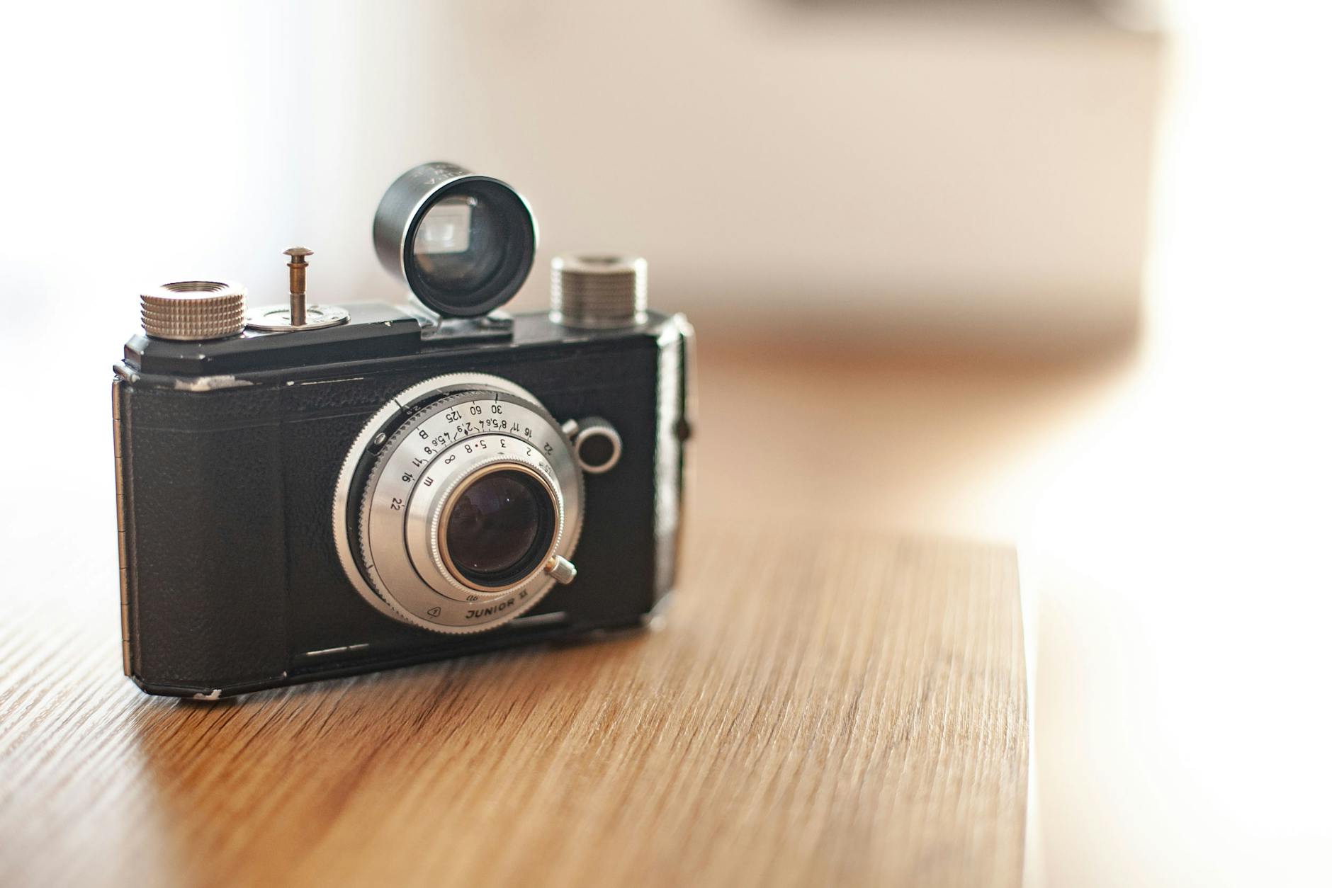 A close-up of a vintage camera on a wooden table, showcasing its classic design and lens.