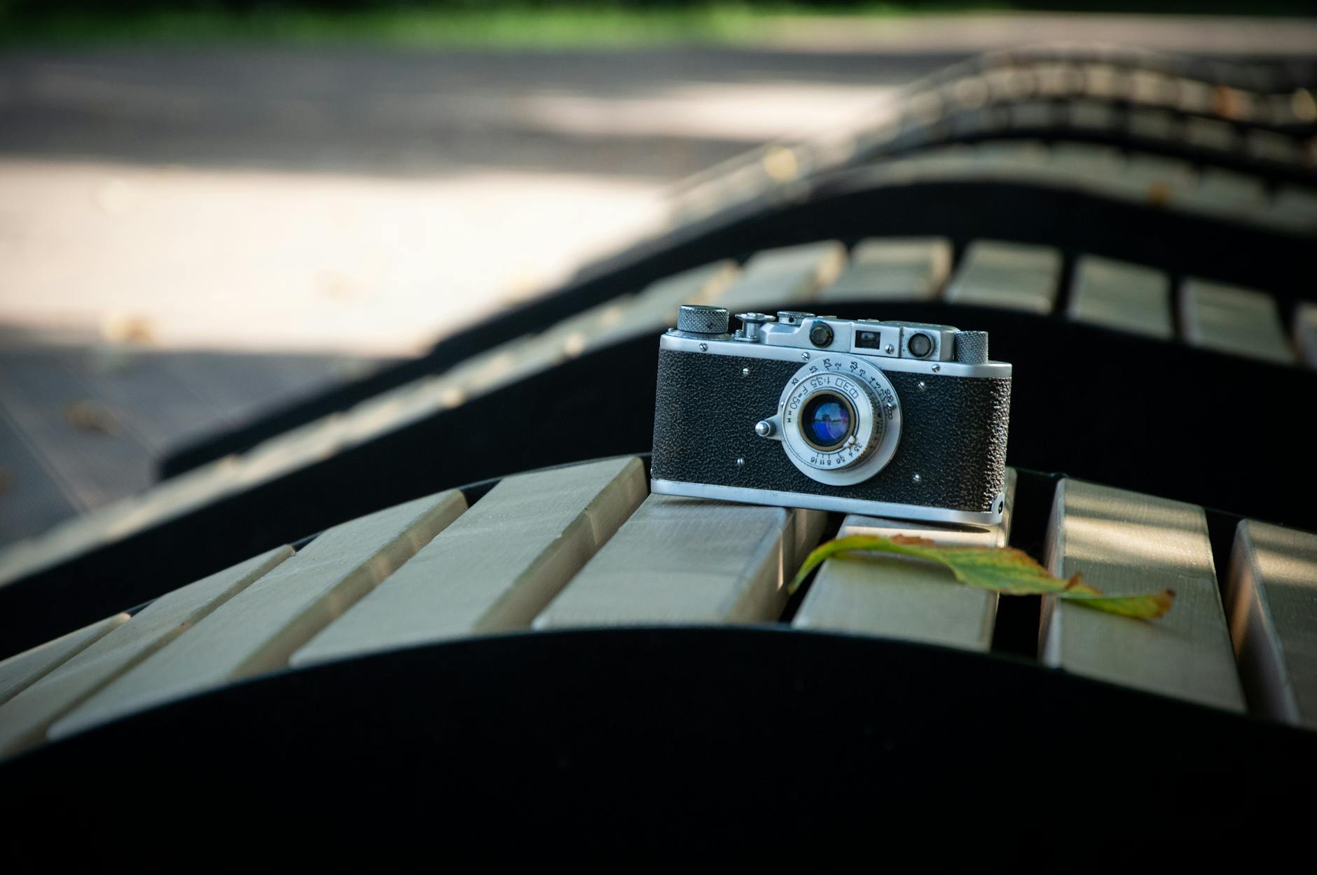 Vintage camera resting on a park bench with scattered leaves in a sunny outdoor setting.