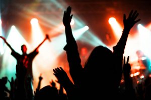 Silhouetted concert crowd captured in vibrant lighting with hands raised in excitement.