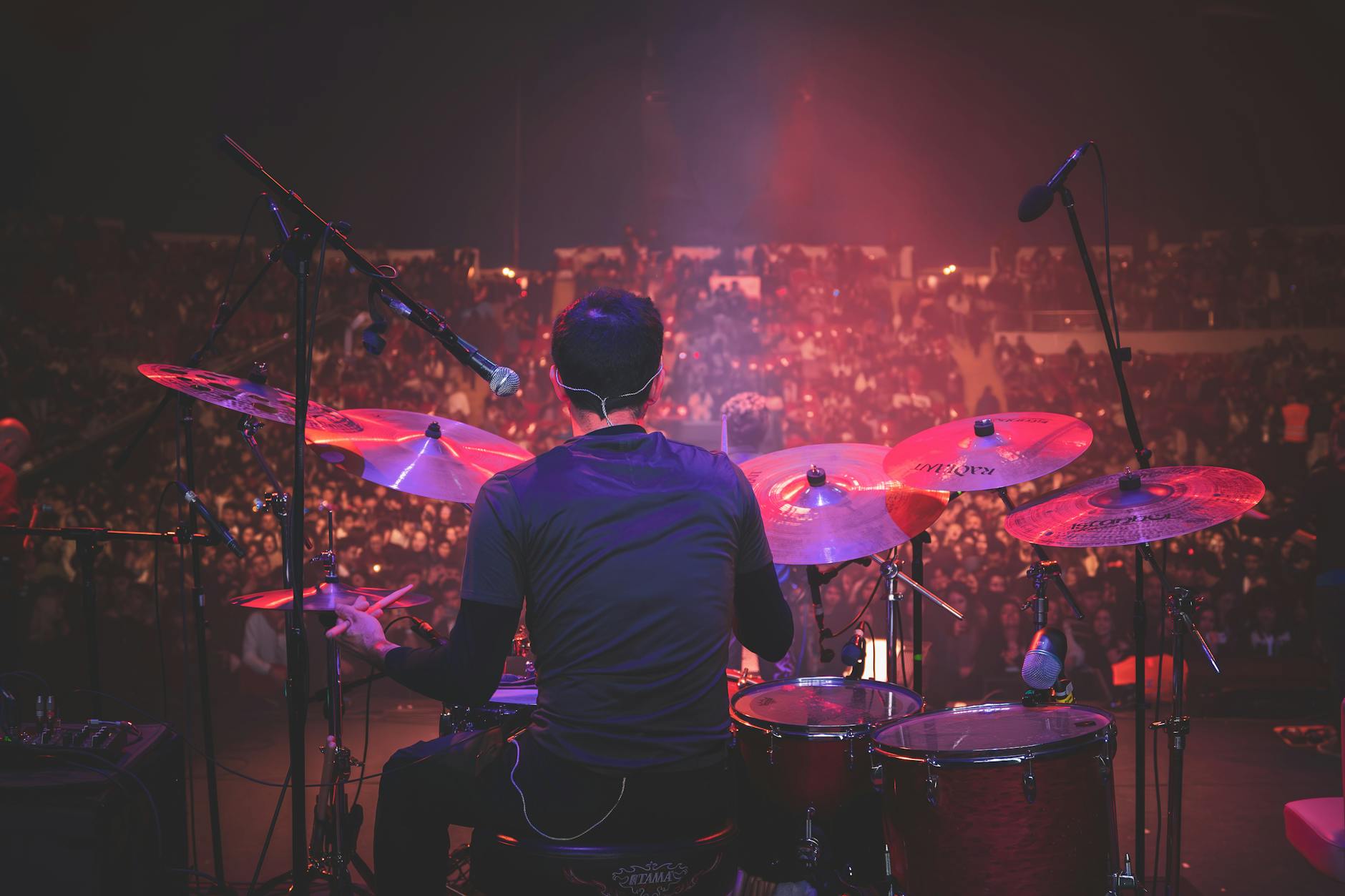 Back view of drummer playing on stage at a live music concert with a packed audience.