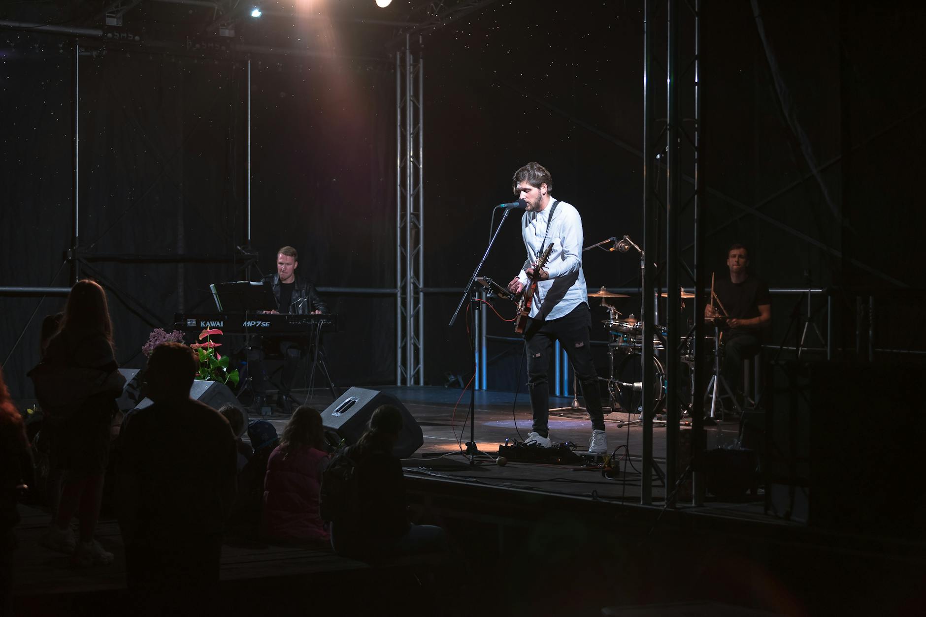 Dynamic band performing live with guitar, keyboard, and drums on an illuminated stage.