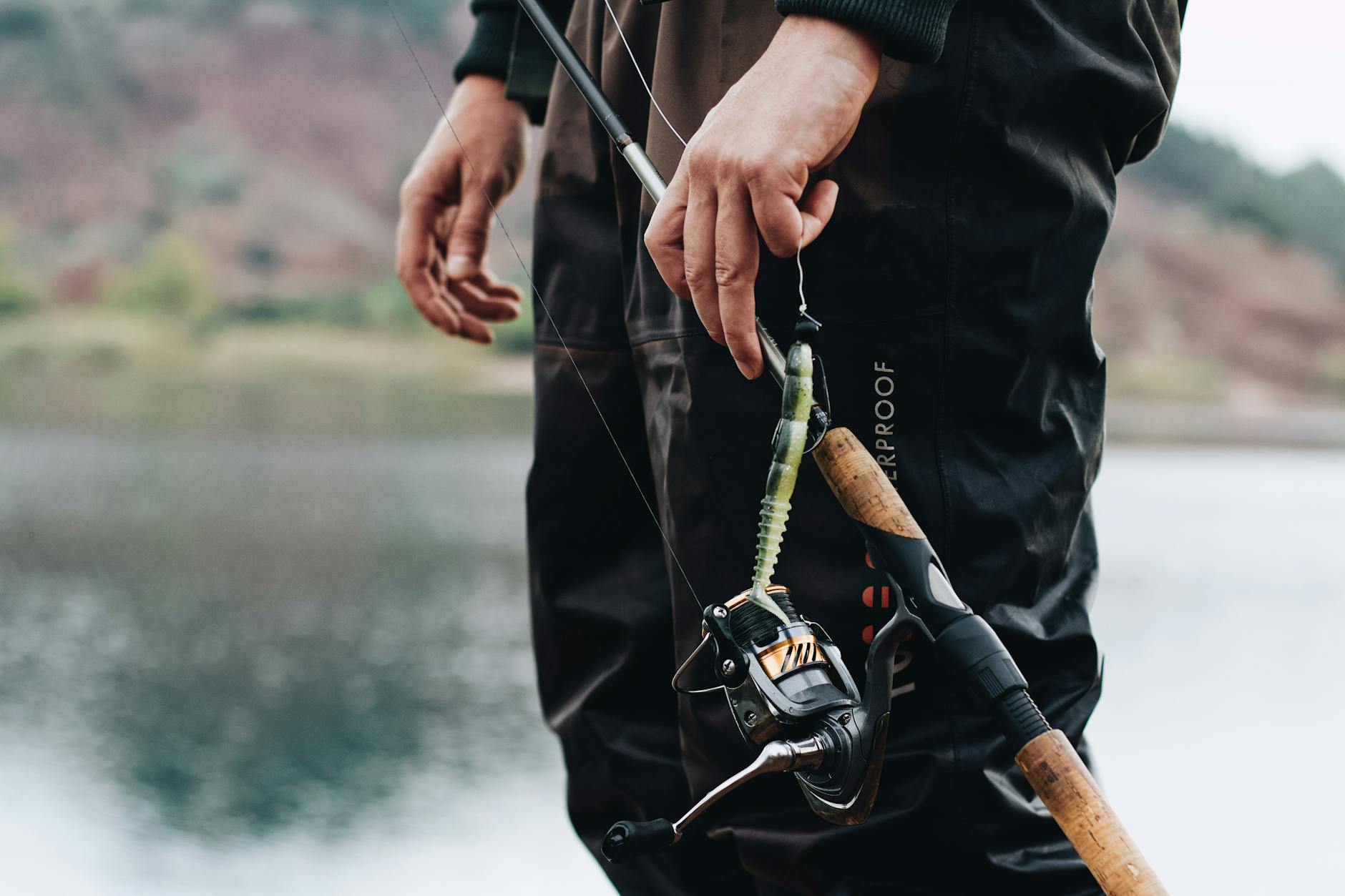 Angler standing by a lake adjusting the fishing rod and bait, ready for a day of fishing.