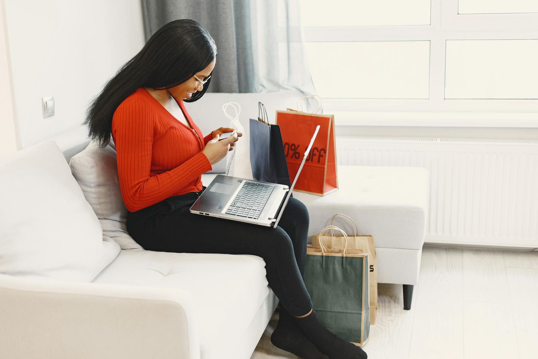 Mixed race woman sits on sofa shopping online with a laptop and shopping bags around.