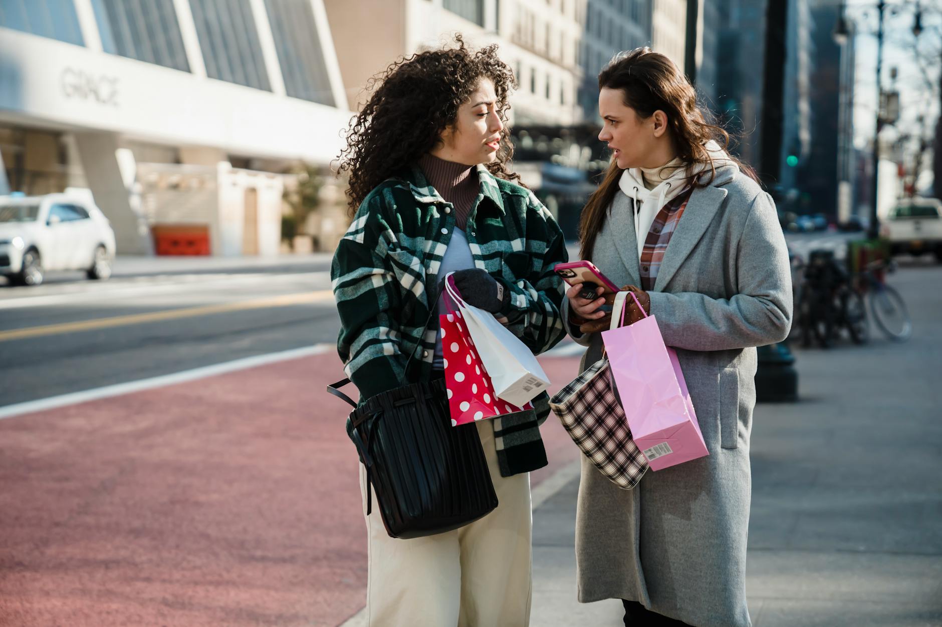 Modern female friends in trendy clothes standing on city street and communicating with each other in daytime