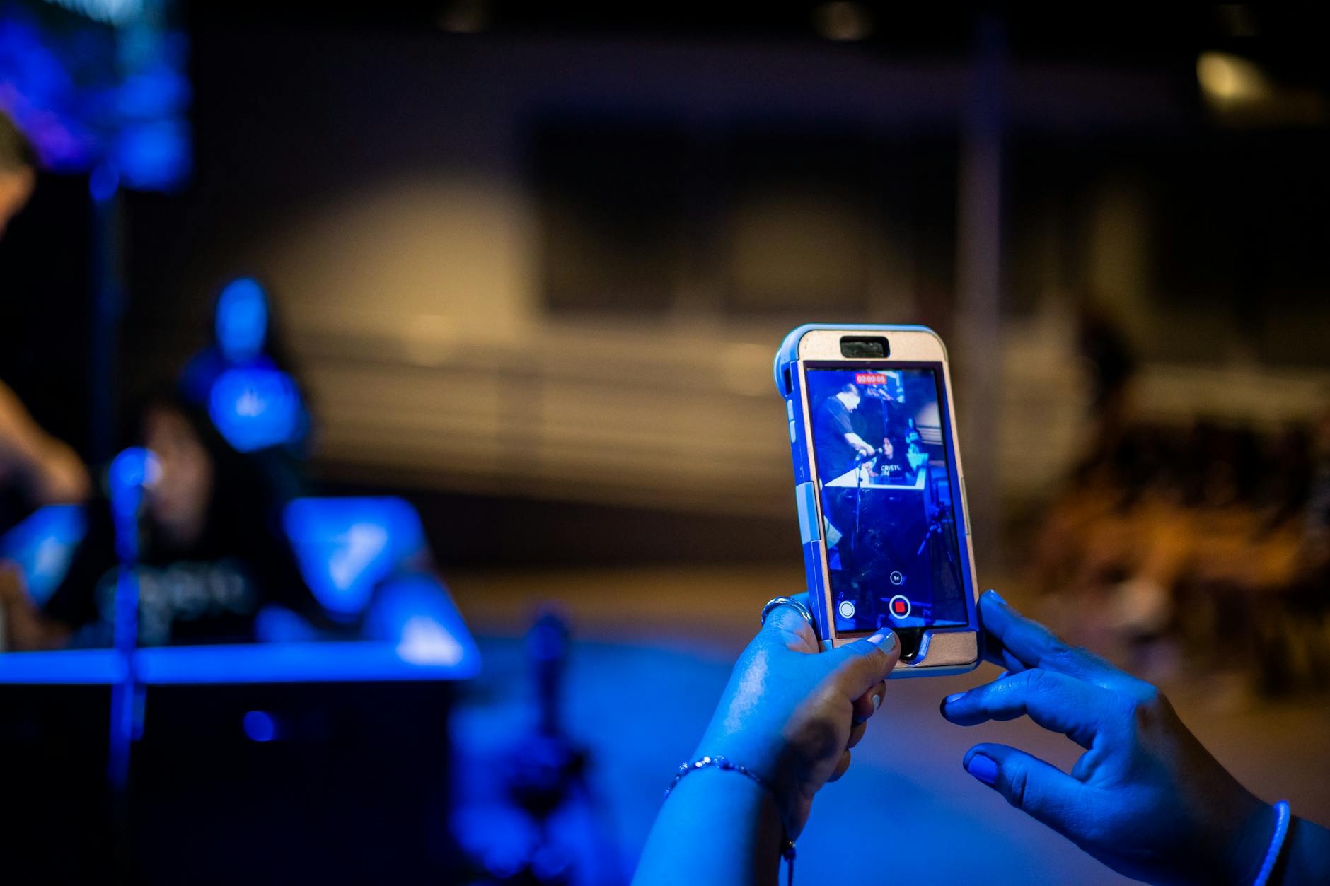 Close-up of hands capturing a scene with a smartphone in a dimly lit environment.