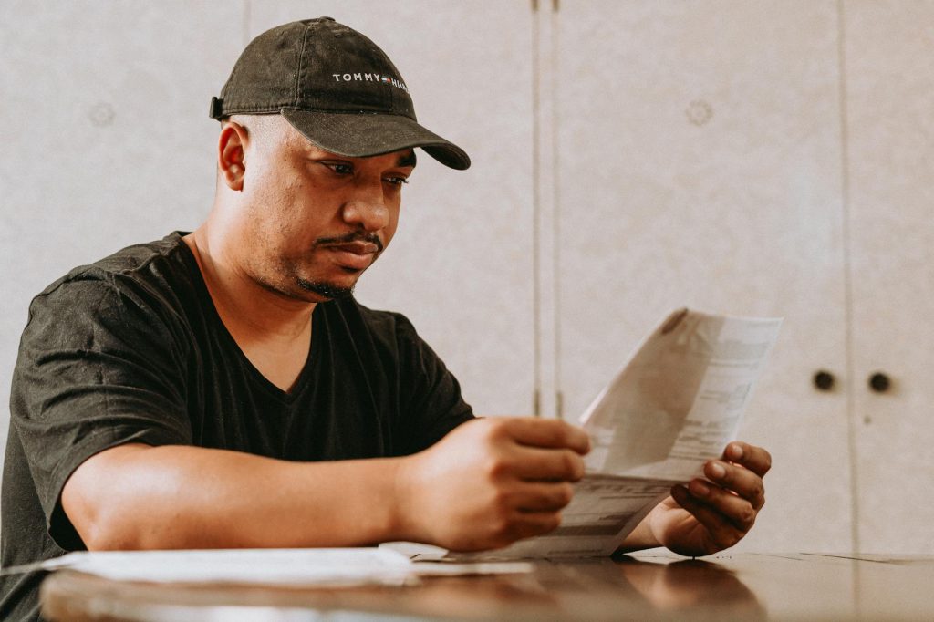 A man in a black cap reading papers at a table indoors.
