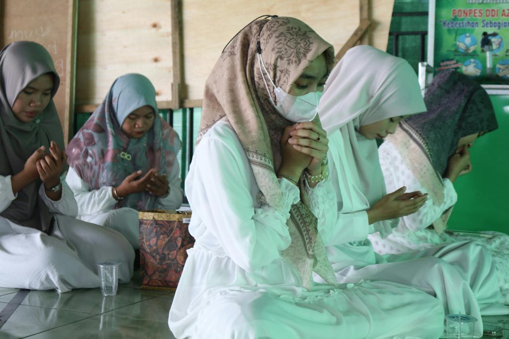 A group of women in hijabs kneeling indoors, focused on prayer and spirituality.