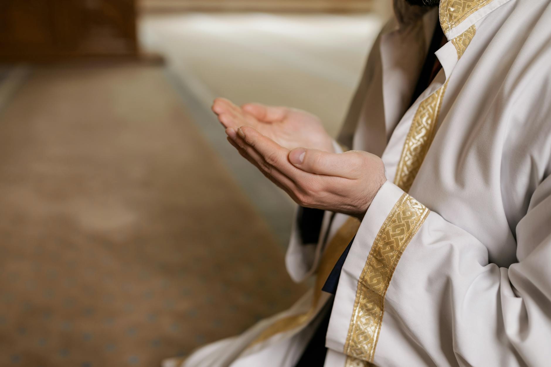 A man in traditional Middle Eastern attire prays indoors, hands clasped together.