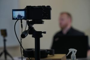 Close-up of camera setup during an indoor filming session with a blurred speaker in the background.