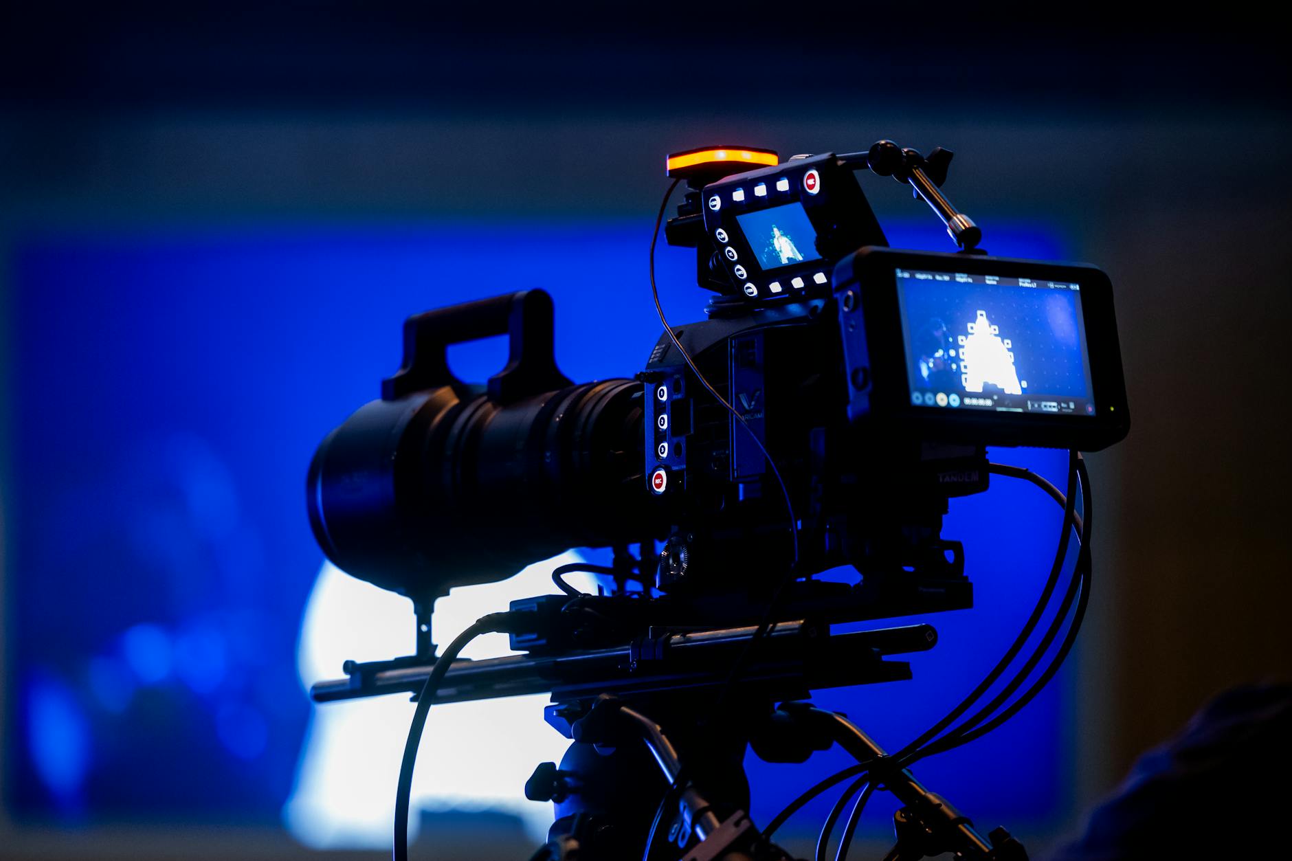 High-end video camera rig in studio setting with auxiliary monitor displays and vibrant blue lighting.