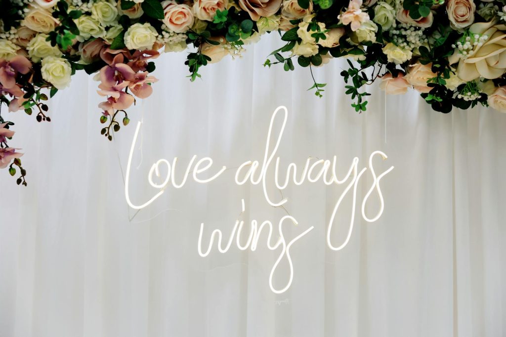 Beautiful floral arrangement with a glowing neon sign reading 'Love always wins'.