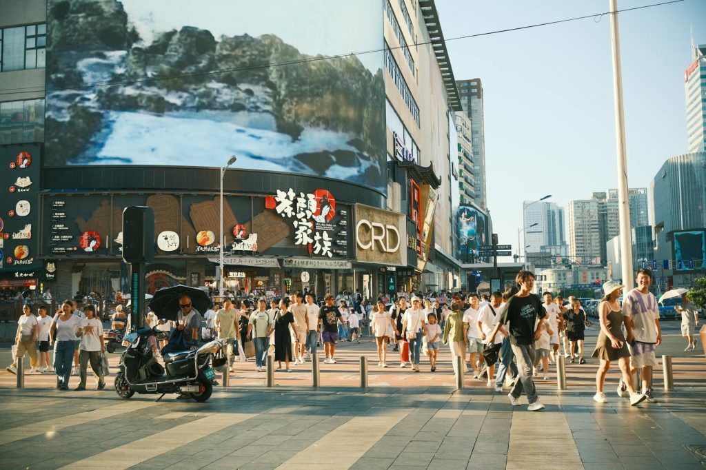 A vibrant urban street filled with people and colorful billboards on a sunny day.
