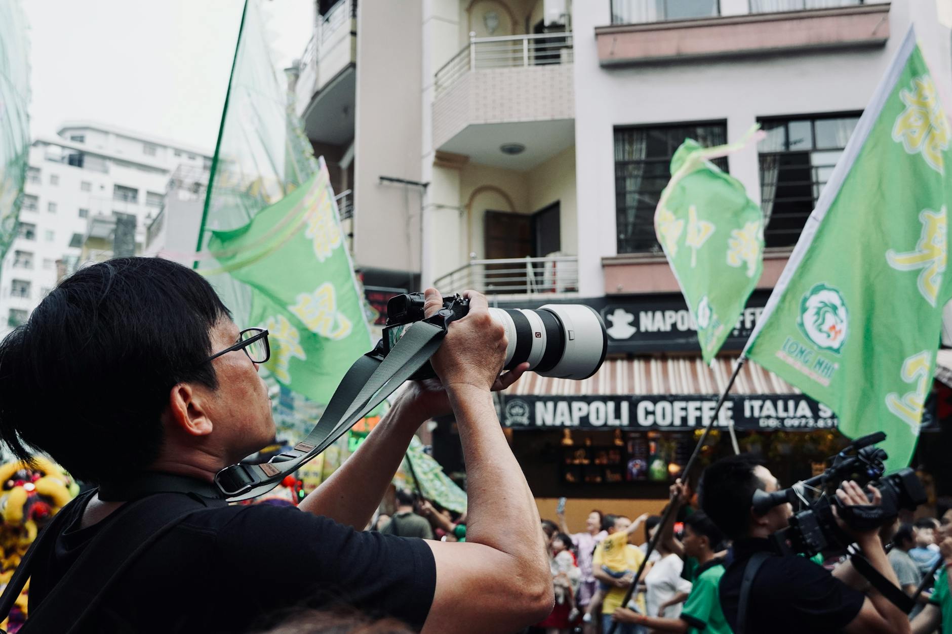 A photographer with a large camera captures a colorful, lively street parade scene.