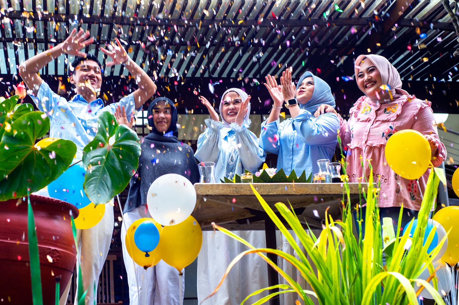 Group of friends celebrating with confetti and balloons in an outdoor setting, creating a festive atmosphere.