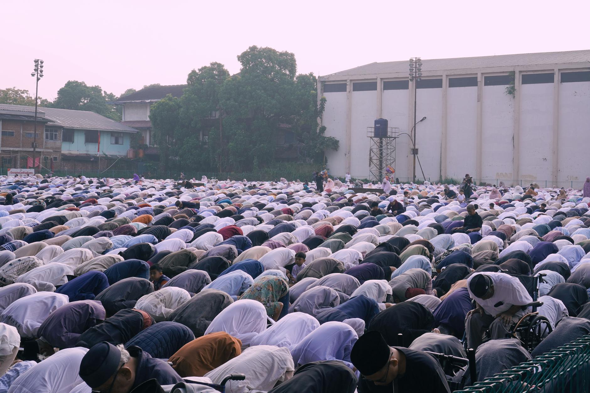 Large group of people gathered outdoors for prayer at dusk. Community, faith, and tradition are highlighted.