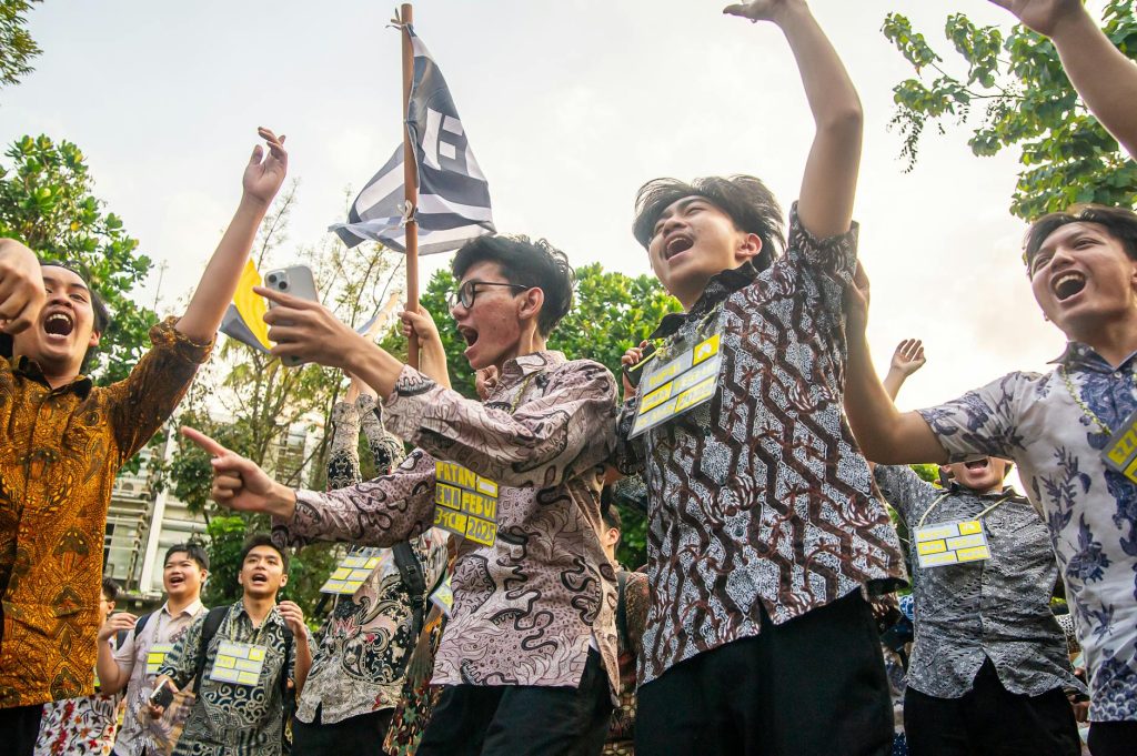 A group of young adults celebrating outdoors with enthusiasm and energy, holding flags and cheering.