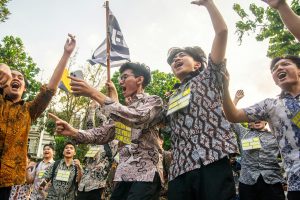 A group of young adults celebrating outdoors with enthusiasm and energy, holding flags and cheering.
