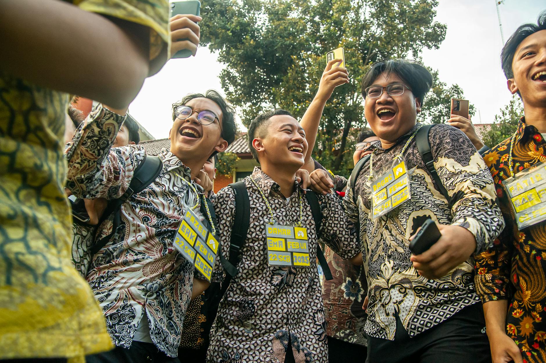 A group of cheerful students in batik shirts celebrating together outdoors.