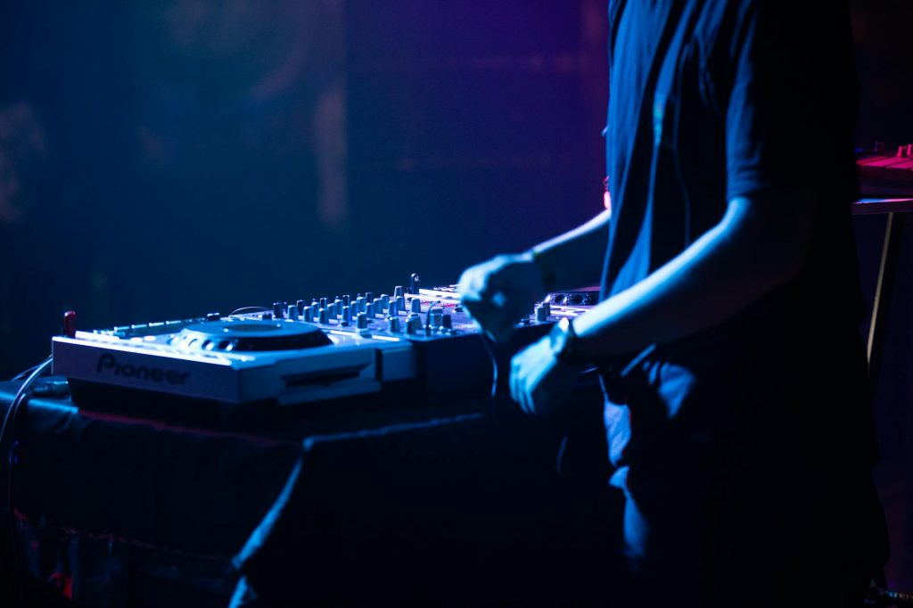 DJ in action adjusting controls on a DJ console during a live performance at a club.