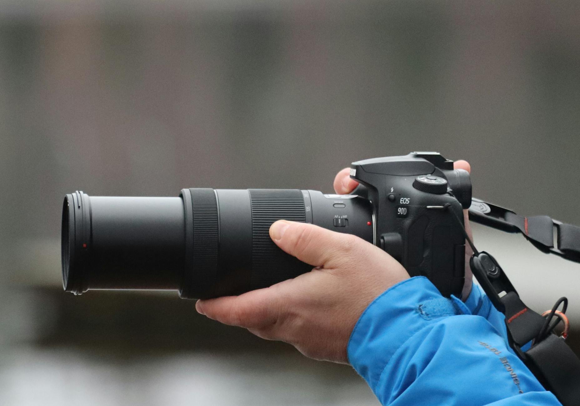 A close-up shot of hands holding a DSLR camera with a telephoto lens, capturing action.