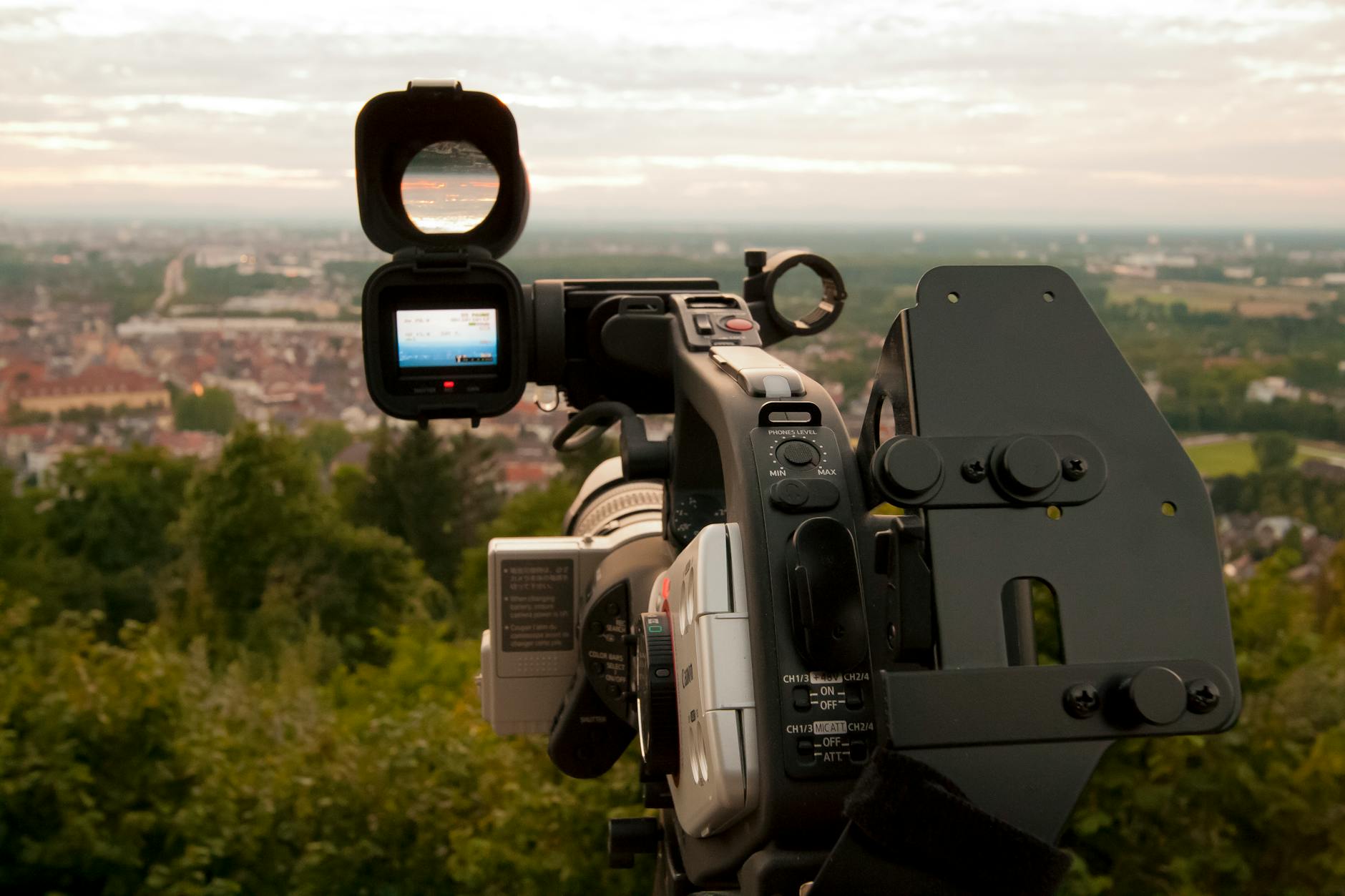 Close-up of a professional video camera set up outdoors with a city skyline in the background.