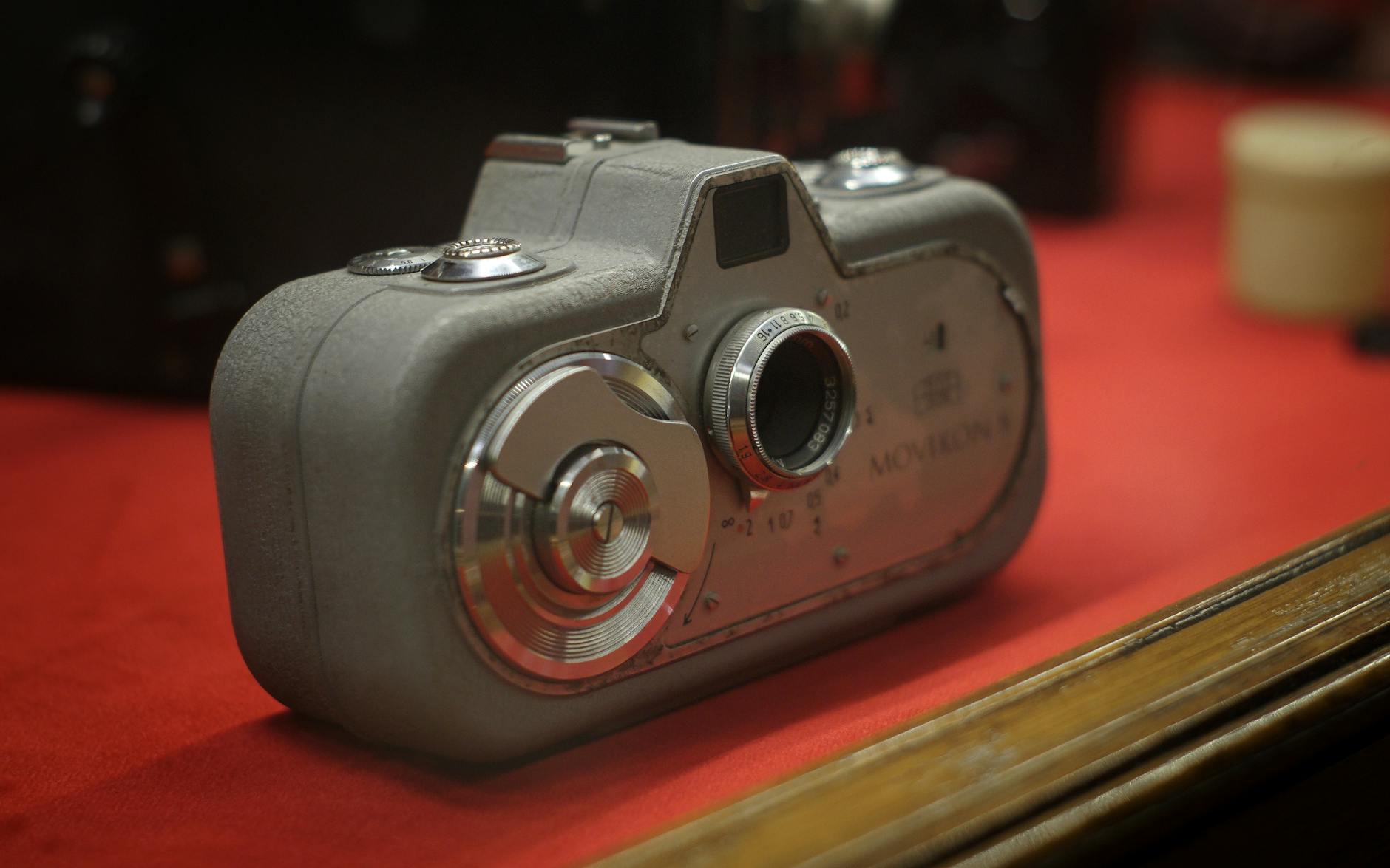 Close-up of a vintage camera on a red background, displayed in a museum setting.