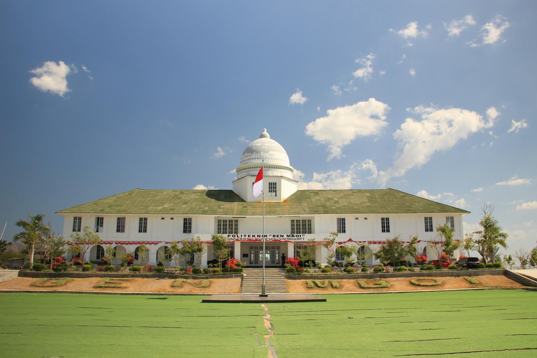 Front view of Politeknik Negeri Kupang under a clear blue sky.
