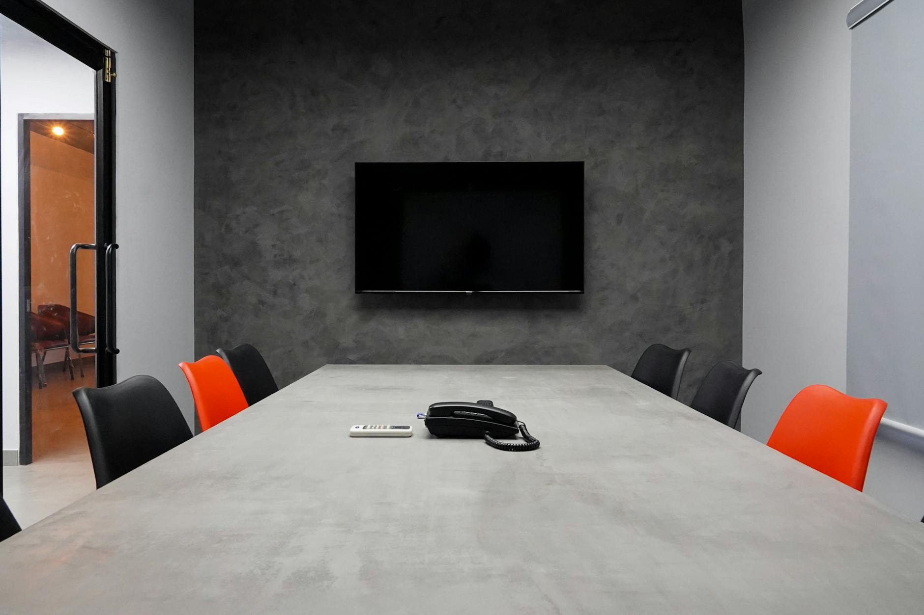 Sleek conference room featuring a large table, black and red chairs, and a wall-mounted TV.