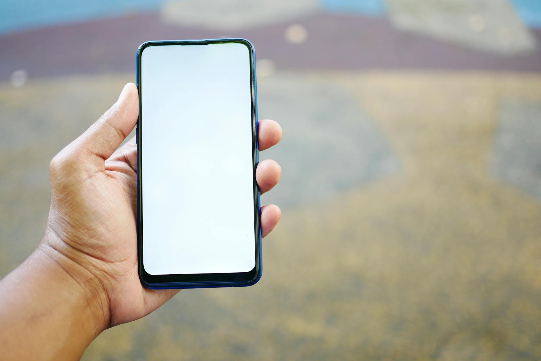A close-up of a hand holding a smartphone with a blank white screen, outdoors.