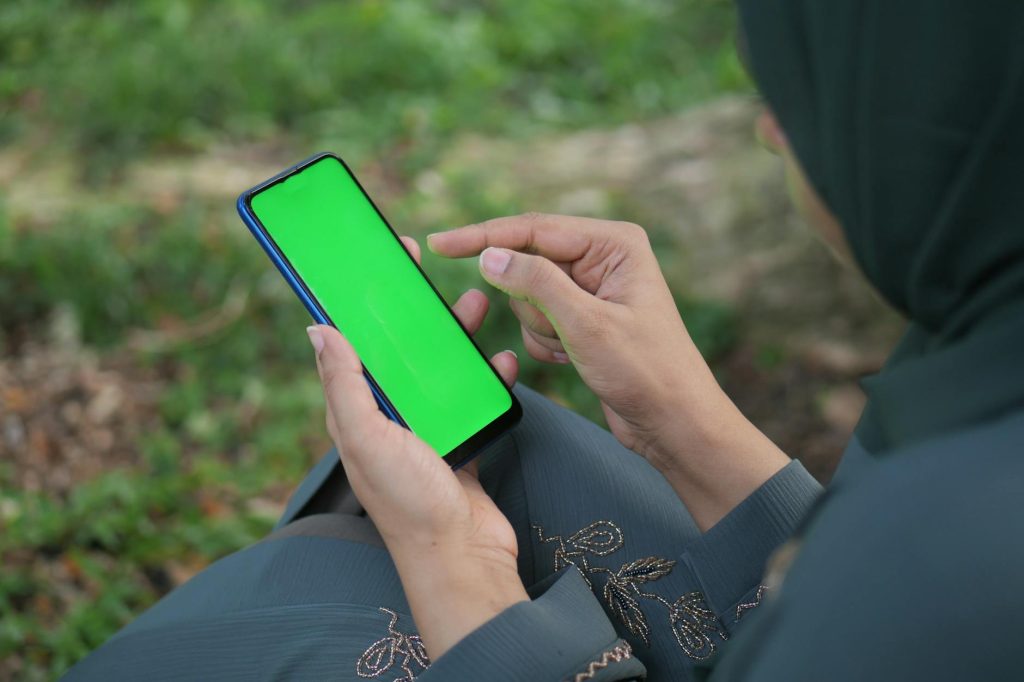 Person holding smartphone with green screen in a natural outdoor setting.