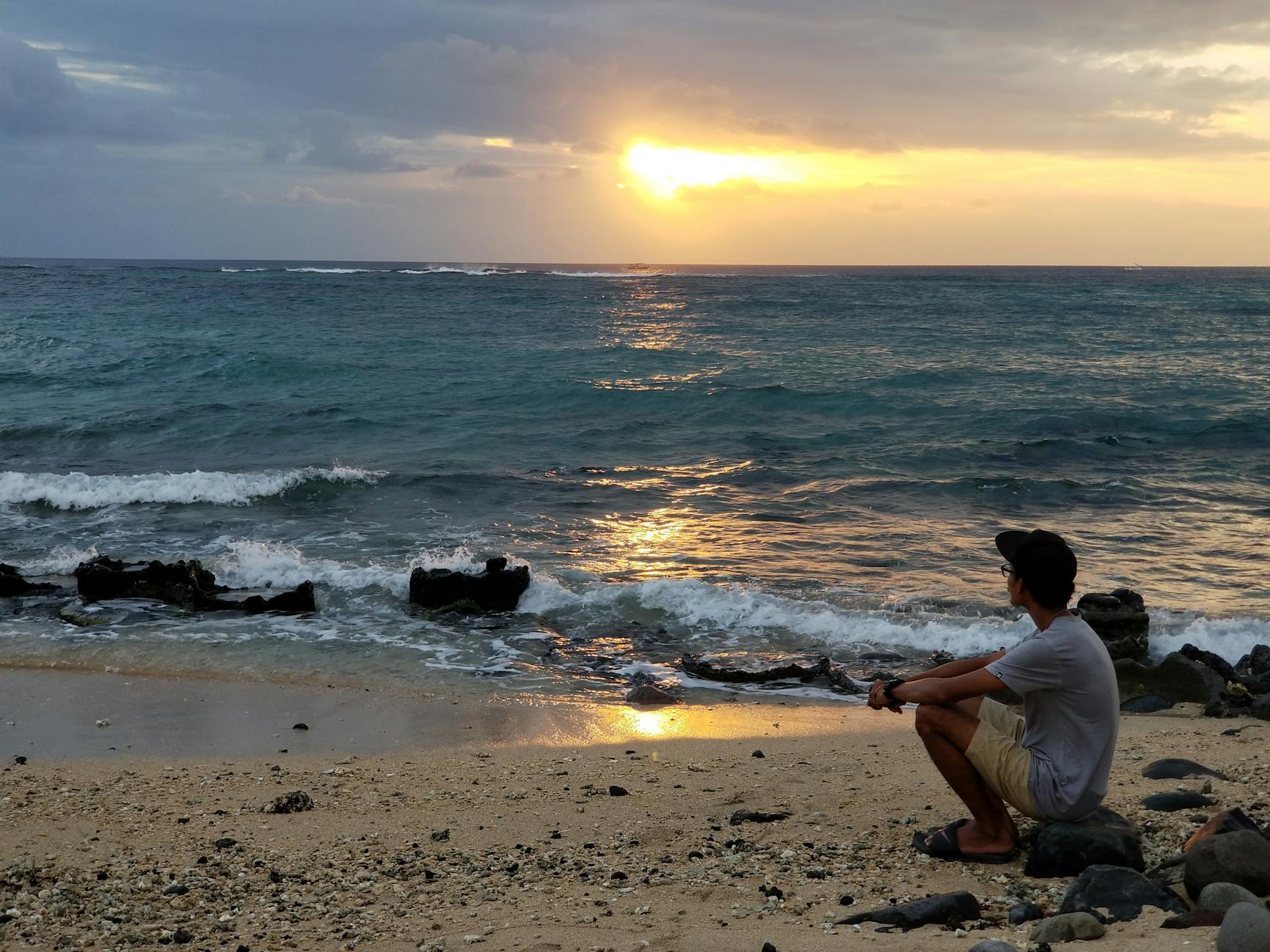 A person enjoys a tranquil sunset at Batu Layar Beach, Indonesia with waves crashing softly on the shore.
