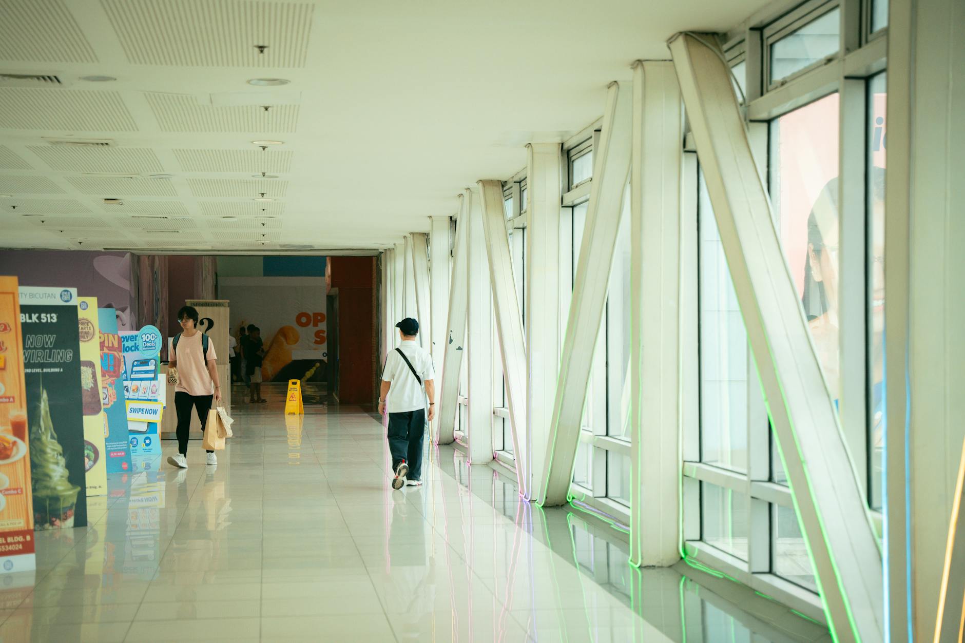 Indoor corridor with natural light, showing people walking and colorful posters. Modern architecture style.