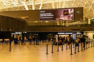 Travelers check in at Zagreb Airport with large advertising screen above.