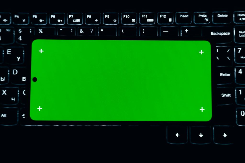 A smartphone with a green screen sits on a lit keyboard, ideal for chroma key editing.