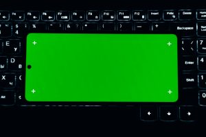A smartphone with a green screen sits on a lit keyboard, ideal for chroma key editing.