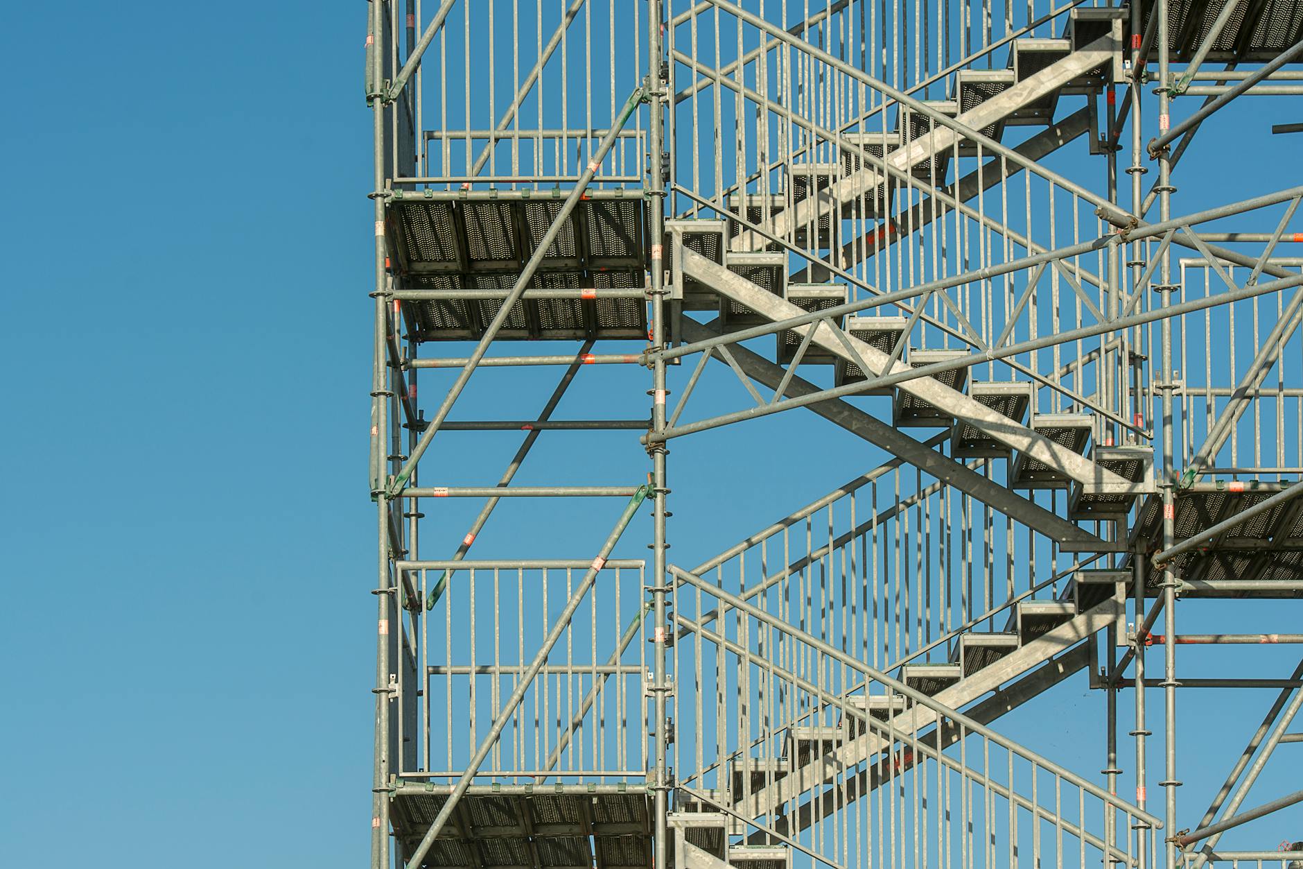 Close-up of metal scaffolding structure with stairs against a clear blue sky, illustrating construction and industrial themes.