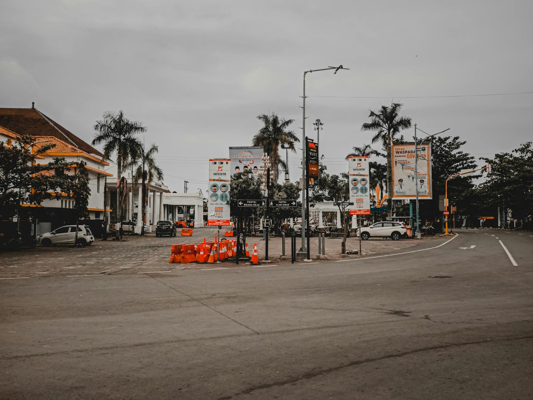 Exterior of tropical town with asphalt roadway with signboards parked automobiles and houses under cloudy sky