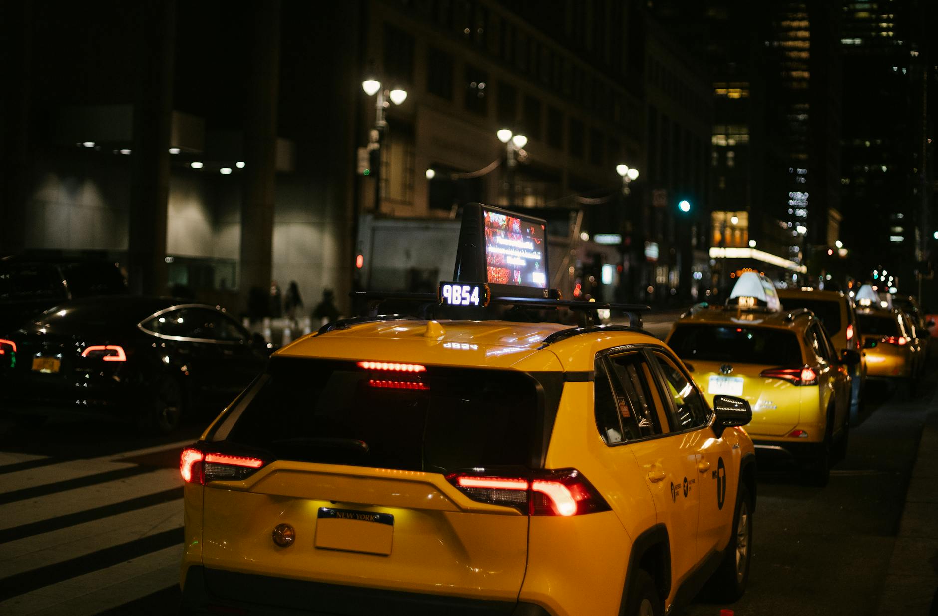 Comfortable yellow crossover taxi cars driving on night city street amidst modern buildings