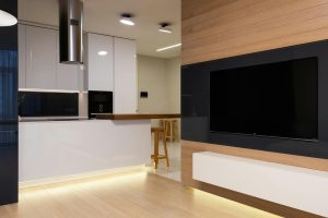 Modern flat with TV set hanging on wall in living room and kitchen furnished with glossy cabinets and shining lamps