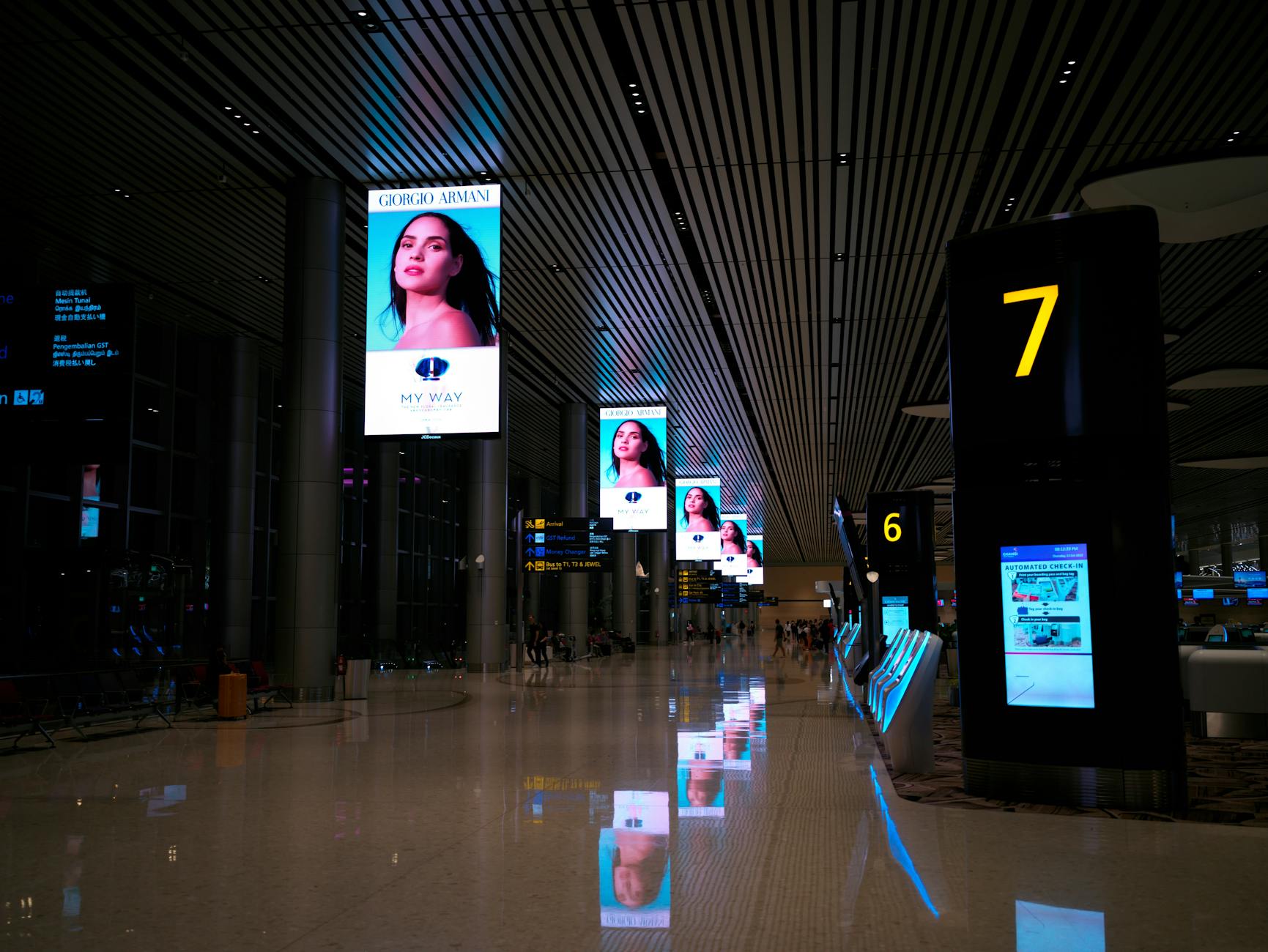 Empty airport hallway with digital displays and glossy floors at night.