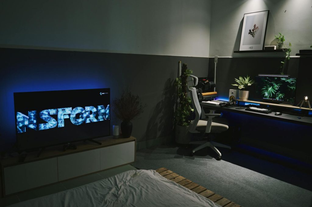 A sleek gaming room featuring a dark, contemporary setup with ambient blue lighting and multiple screens.
