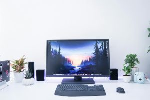Contemporary desk setup featuring a monitor, plants, and electronic devices in a sleek, minimalist design.