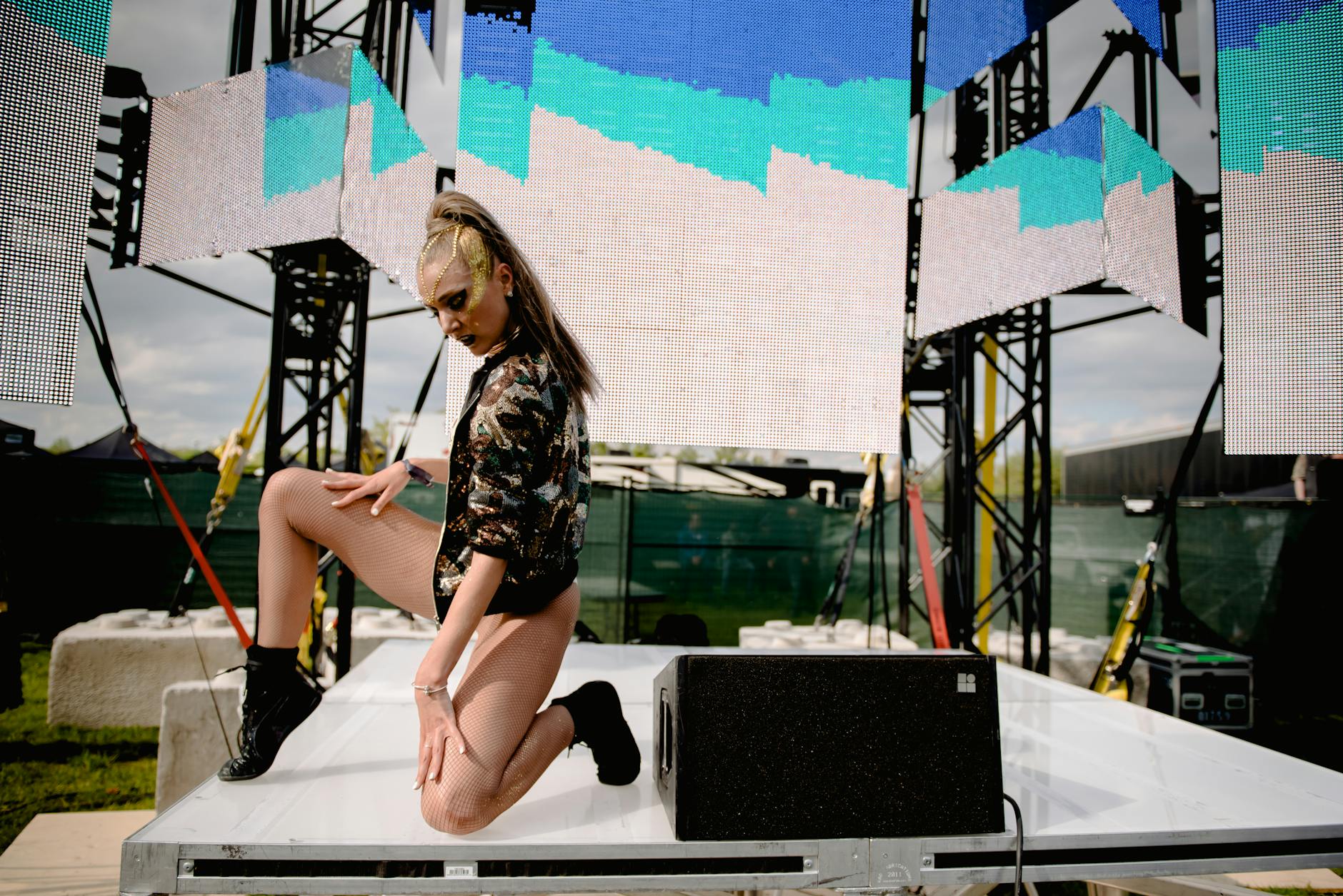 A fashionable performer striking a pose on an outdoor stage with vibrant digital displays.