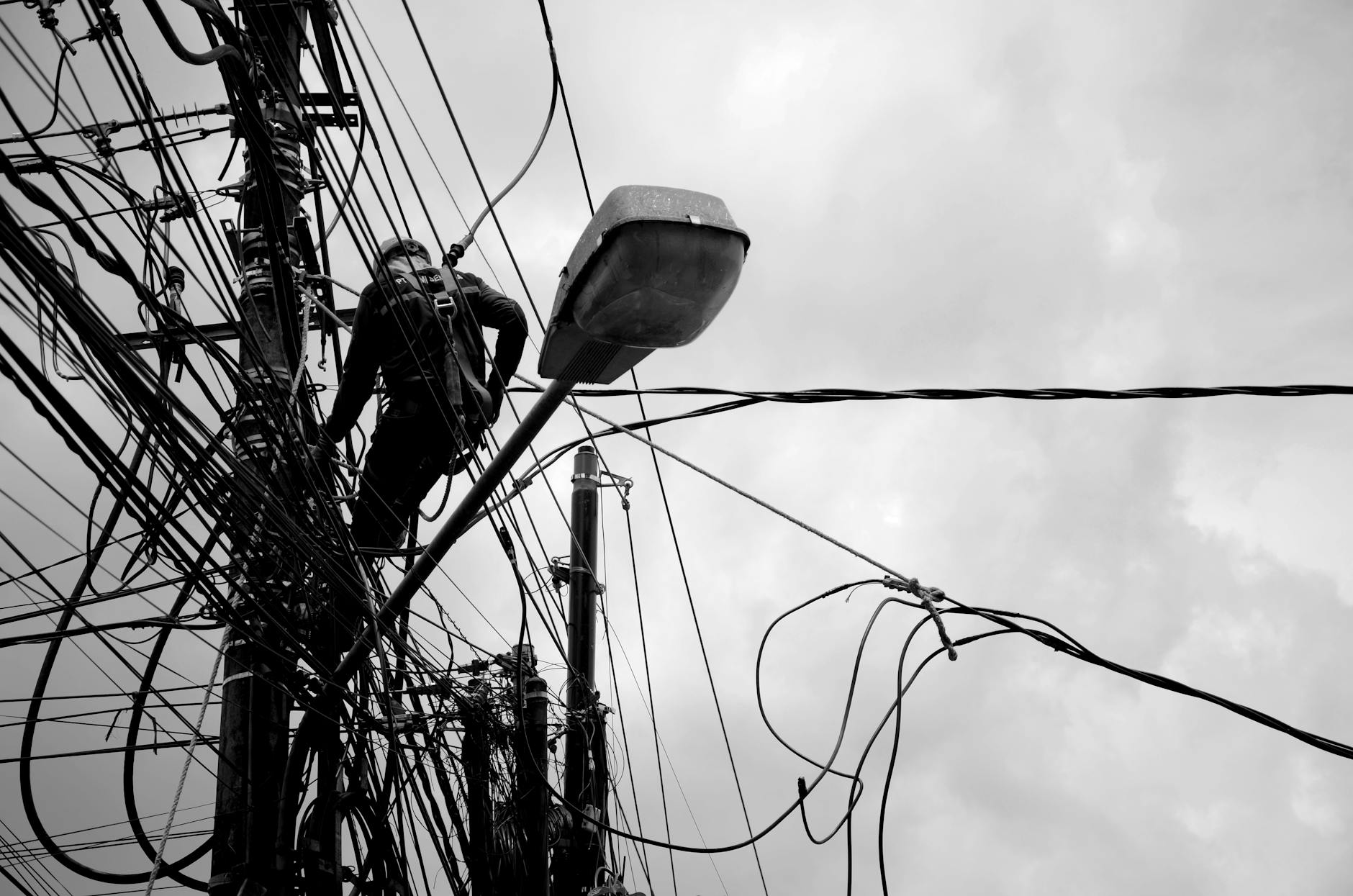 Black and white image of a technician working on power lines, illustrating electrical repair work.